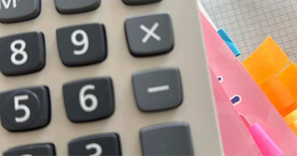 電卓の下に付箋を貼ったテキストが積んである画像